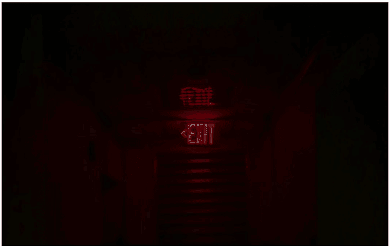 A dimly lit emergency exit sign glowing red in a dark hallway, illustrating the importance of circuit integrity fire cables in maintaining fail-safe system protection during emergencies